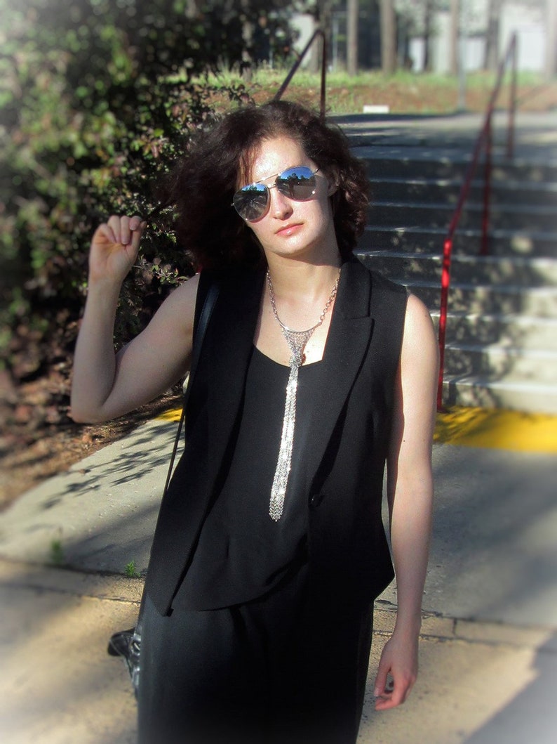 Puede incluir: Una mujer con un chaleco negro sin mangas, un collar de cadena plateada y gafas de sol. Est&aacute; de pie en una escalera.