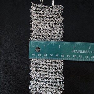 May include: A silver wire mesh bracelet with a textured, woven design. The bracelet is approximately 3 inches long and is measured against a ruler.