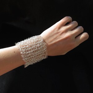 May include: A silver wire bracelet with a delicate, open-weave design. The bracelet is worn on a person's wrist.
