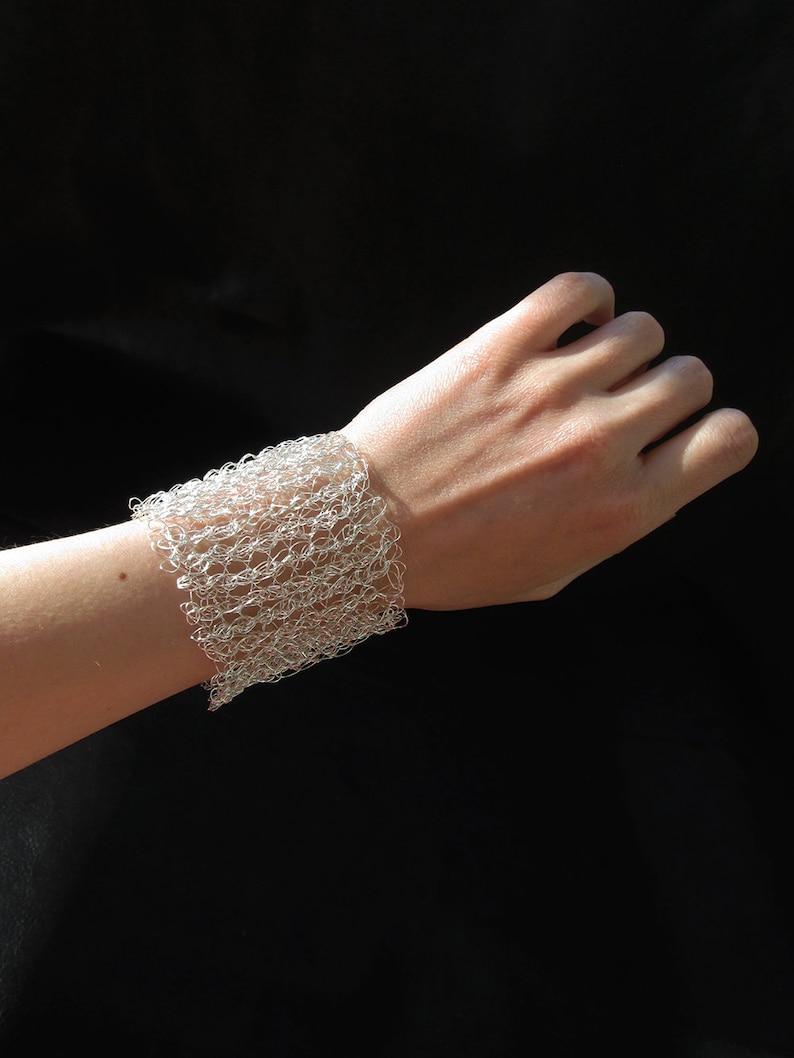 May include: A silver wire bracelet with a delicate, open-weave design. The bracelet is worn on a person's wrist.