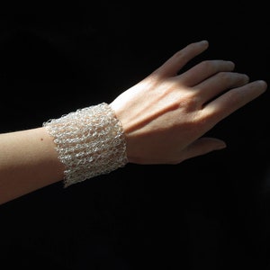 May include: A silver wire mesh bracelet on a person's wrist. The bracelet is made of small, interconnected loops of wire, creating a delicate and airy design.