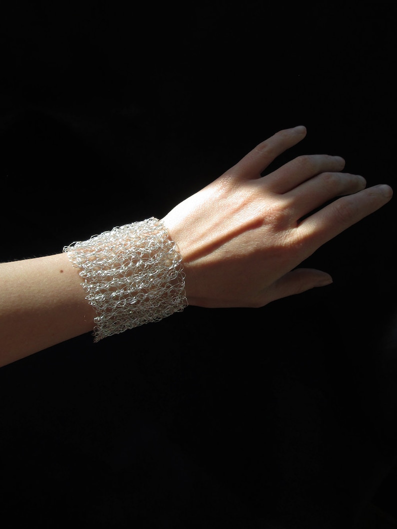 May include: A silver wire mesh bracelet on a person's wrist. The bracelet is made of small, interconnected loops of wire, creating a delicate and airy design.