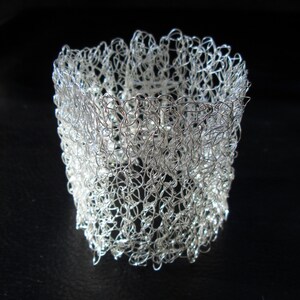 May include: A silver wire bracelet with a delicate, crocheted design. The bracelet is made of thin, interwoven wire that creates a lacy, openwork pattern.