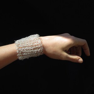 May include: A silver wire mesh bracelet on a person's wrist. The bracelet is made of small, interconnected loops of wire.