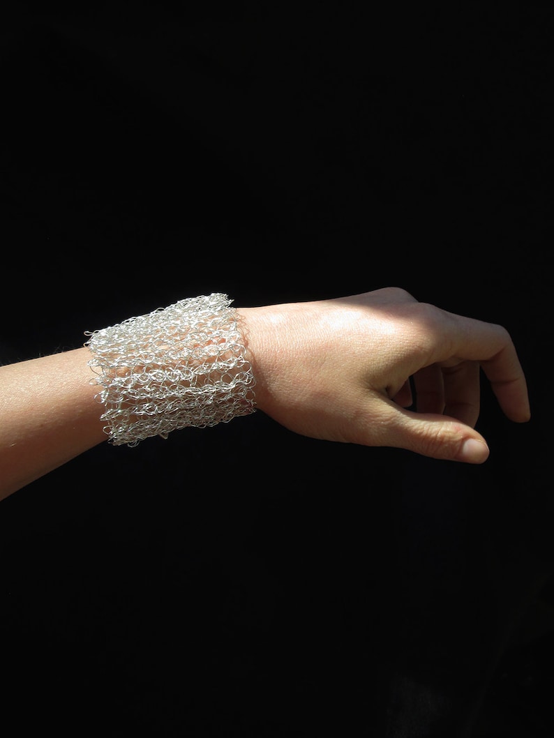 May include: A silver wire mesh bracelet on a person's wrist. The bracelet is made of small, interconnected loops of wire.