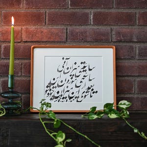 Pu&ograve; includere: Una candela verde accesa in un portacandele di vetro verde scuro &egrave; accanto a un'opera d'arte calligrafica incorniciata. L'arte presenta una scritta nera su sfondo bianco, incorniciata in una cornice marrone chiaro. Lo sfondo &egrave; un muro di mattoni.
