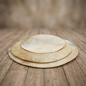 Peut inclure: Trois pièces circulaires, plates et fines de peau animale beige clair, semi-translucide, empilées les unes sur les autres. Chaque pièce présente une texture naturelle et inégale avec des variations de couleur subtiles, allant du crème au brun clair.