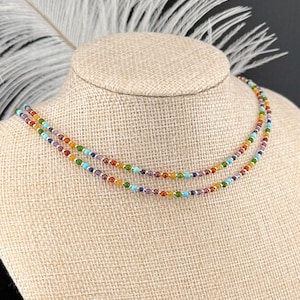 May include: Two delicate necklaces with colorful beads are displayed on a mannequin. The necklaces feature a rainbow of colors, including red, orange, yellow, green, blue, and purple. The beads are small and evenly spaced, creating a vibrant and eye-catching accessory.