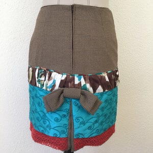 Pode incluir: Uma saia pelo joelho com um padr&atilde;o de p&eacute;-de-galinha castanho e bege na parte superior, um la&ccedil;o central de p&eacute;-de-galinha castanho, uma faixa com folhos em estampado floral castanho, branco e turquesa, um painel bordado turquesa e uma bainha de renda vermelha.