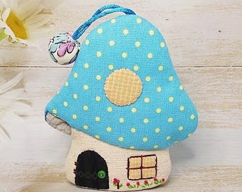 May include: A blue and white polka dot mushroom-shaped fabric house with a small door and window. The house is decorated with a yellow circle and red flowers.