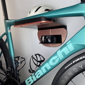 Può includere: Una bici da corsa Bianchi turchese con una mensola a muro nera e color rame. La mensola contiene un casco bianco e occhiali da sole. La bici ha ruote nere e un portaborraccia.