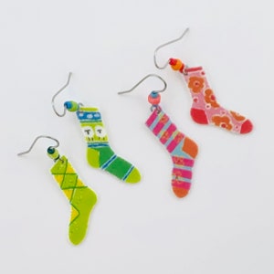 May include: Three pairs of sock-shaped earrings. One pair is green with a diamond pattern, one pair is green with a white and blue pattern, and one pair is pink with a floral pattern.
