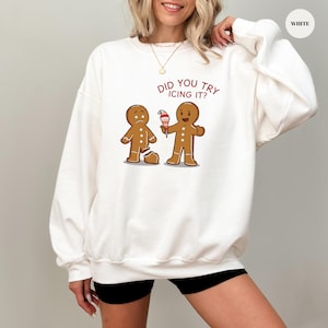 Könnte beinhalten: Weißes Sweatshirt mit einem humorvollen Lebkuchenmann-Motiv. Ein Lebkuchenmann hat ein gebrochenes Bein, der andere hält ein Eis. Der Text "DID YOU TRY ICING IT?" ist rot.