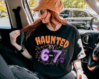 May include: Black t-shirt with the text "HAUNTED BY 6-7" in orange and purple. The design includes stars and a ghost graphic. The person in the image is wearing a corduroy hat and sunglasses.