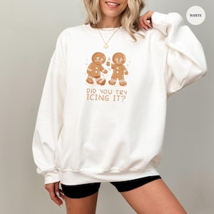 May include: White sweatshirt with a gingerbread man graphic. The design features two gingerbread men, one looking sad and the other holding a bottle. The text on the sweatshirt says, "DID YOU TRY ICING IT?"