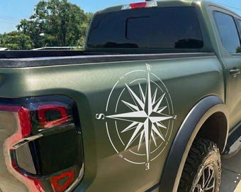 May include: A green pickup truck with a large white compass rose decal on the side. The compass rose is a navigational tool with directional points. The truck has black tires and a black fender.