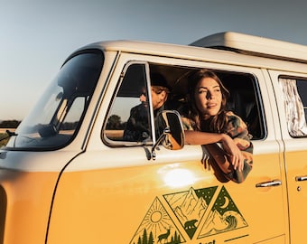 May include: A yellow and white vintage van with a "Wanderlust" decal featuring a sun, mountains, and a bear. A person leans out the window, looking towards the horizon. The van is parked outdoors on a sunny day.
