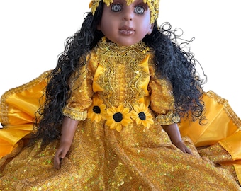 May include: A doll with dark skin, dressed in a yellow sequined gown and a matching headpiece decorated with sunflowers. The doll has long black hair and blue eyes. The dress has a sunflower belt.