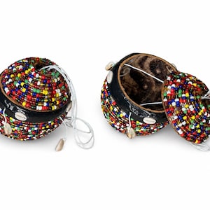 Peut inclure: Deux récipients ronds fabriqués à partir de coques de noix de coco, l'un fermé et l'autre ouvert. L'extérieur est recouvert de perles de verre multicolores et orné de petits coquillages cauris blancs. Une ficelle blanche est fixée au couvercle.
