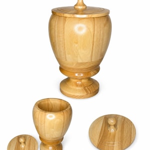 May include: A light brown wooden urn with a matching lid featuring a knob handle. The urn has a rounded body and a pedestal base. Also shown are a separate smaller wooden container and its matching lid, both displaying natural wood grain patterns.