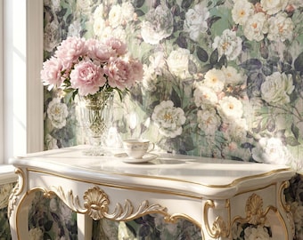 May include: A white console table with gold trim and carved shell details, featuring a clear crystal vase filled with pink peonies and a small white teacup with a saucer, set against a wall covered in floral wallpaper with white roses.
