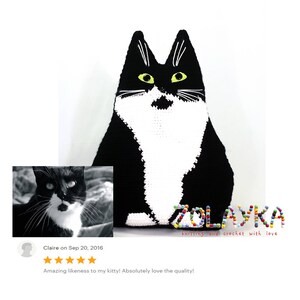 K&ouml;nnte beinhalten: Schwarz-wei&szlig;es geh&auml;keltes Katzenkissen mit gelben Augen. Das Kissen liegt auf einer wei&szlig;en Oberfl&auml;che. Der Text "ZOLAYKA knitting and crochet with love" befindet sich unter dem Kissen.