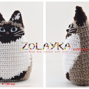 A crocheted cat toy in white and brown. The cat is sitting up and looking to the right. The cat is 10 1/2 inches tall and 8 inches wide. The cat is made by ZOLAYKA knitting and crochet with love.