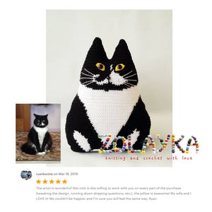 K&ouml;nnte beinhalten: Ein schwarzes und wei&szlig;es geh&auml;keltes Katzenkissen mit gelben Augen. Das Kissen liegt auf einer wei&szlig;en Oberfl&auml;che. Der Text "ZOLAYKA knitting and crochet with love" befindet sich unter dem Kissen.