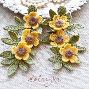 Close-up of delicate yellow buttercup crochet flowers with fine green leaves on gold stud earrings
