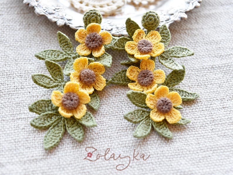 Close-up of delicate yellow buttercup crochet flowers with fine green leaves on gold stud earrings