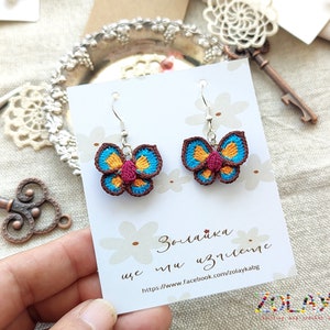 May include: Crocheted butterfly earrings in brown, blue, yellow, and pink on a white card with the text "Zolajka she is the art" and a website address.