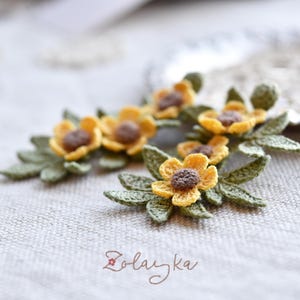 Close-up of delicate yellow buttercup crochet flowers with fine green leaves on gold stud earrings