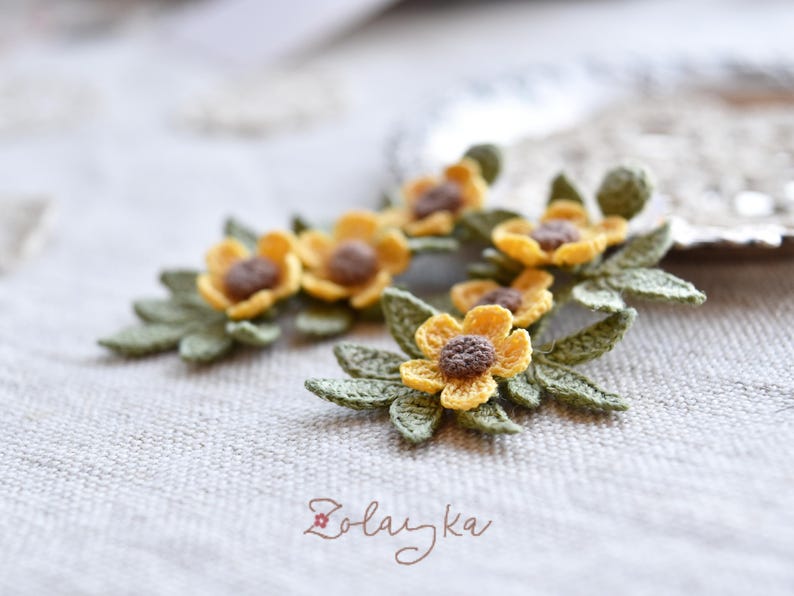 Close-up of delicate yellow buttercup crochet flowers with fine green leaves on gold stud earrings