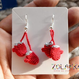 May include: A pair of red crocheted mitten earrings with silver accents hanging from silver hooks. The earrings are displayed on a white card with the text "ZOLANKA knitting and crochet with love".