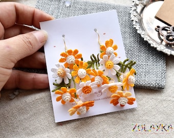May include: A pair of crocheted daisy earrings with yellow and white flowers. The earrings are on a white card with the text "Zolayka" and a website address.