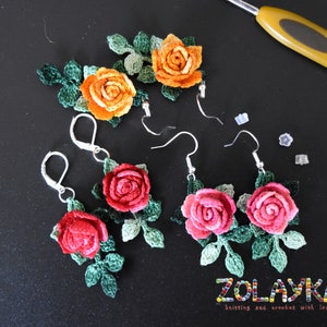May include: Crocheted rose earrings in orange, pink and red with green leaves. The earrings are handmade and feature silver hooks.