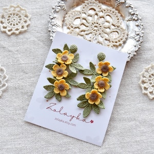 Handmade micro crochet buttercup earrings with yellow flowers and green leaves on gold plated studs. Flat lay of micro crochet buttercup earrings with bright yellow blossoms and green leaves on white background.