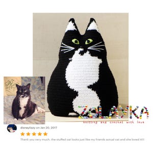 K&ouml;nnte beinhalten: Ein schwarzes und wei&szlig;es geh&auml;keltes Katzenkissen mit gr&uuml;nen Augen. Das Kissen liegt auf einer hellbraunen Oberfl&auml;che. Der Text "SZOLASKA knitting and crochet with love" befindet sich unter dem Kissen.