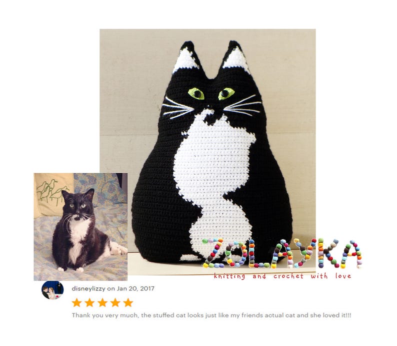 K&ouml;nnte beinhalten: Ein schwarzes und wei&szlig;es geh&auml;keltes Katzenkissen mit gr&uuml;nen Augen. Das Kissen liegt auf einer hellbraunen Oberfl&auml;che. Der Text "SZOLASKA knitting and crochet with love" befindet sich unter dem Kissen.