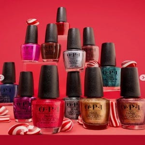 May include: A collection of OPI nail lacquer bottles in various colors, including pink, brown, silver, teal, gold, and red, arranged on a red surface. The bottles have black caps and are accompanied by candy canes and peppermint candies.