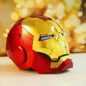 Può includere: Un casco di Iron Man metallico e lucido con una vivace combinazione di colori rosso e oro. Il casco presenta una finitura liscia e riflettente con linee di pannello modellate, una piastra frontale dorata e fessure scure per gli occhi.