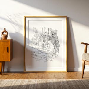 May include: A framed black and white architectural print depicting a cityscape with construction workers. The artwork is in a gold frame and leans against a white wall. A wooden cabinet and chair are visible.