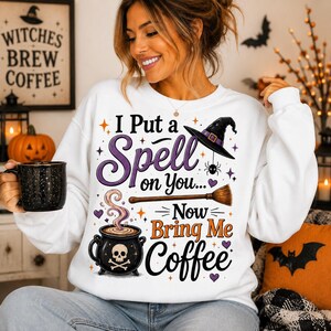 Può includere: Una felpa bianca a maniche lunghe con una stampa grafica che riporta il testo I Put a Spell on You... Now Bring Me Coffee, un cappello da strega nero, una scopa e un calderone nero con un disegno di teschio e vapore che si sprigiona.