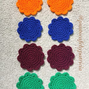 May include: Eight round, scalloped-edge crochet coasters arranged in two columns. The colors include two orange, two blue, two dark purple, and two green coasters. The text "@puntocafebypatricia" is printed vertically along the right side.