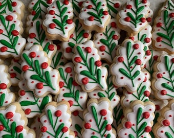 Puede incluir: Primer plano de una pila de galletas de Navidad decoradas con hojas verdes y bayas rojas.