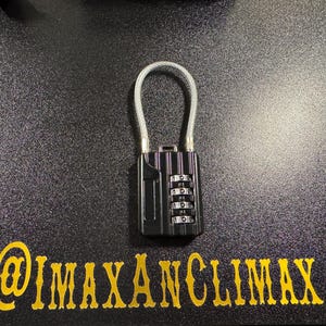 May include: Black combination lock with a silver cable loop. The lock has four number dials and is set against a textured black surface. The text "@IMAXANCLIMAX" is in gold lettering below the lock.