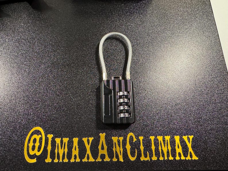 May include: Black combination lock with a silver cable loop. The lock has four number dials and is set against a textured black surface. The text "@IMAXANCLIMAX" is in gold lettering below the lock.