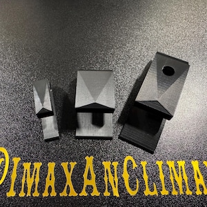 May include: Three black geometric objects with a faceted top and a rectangular base are displayed on a textured black surface. One object has a hole. The text "@IMAXANCLIMAX" is in gold script at the bottom.