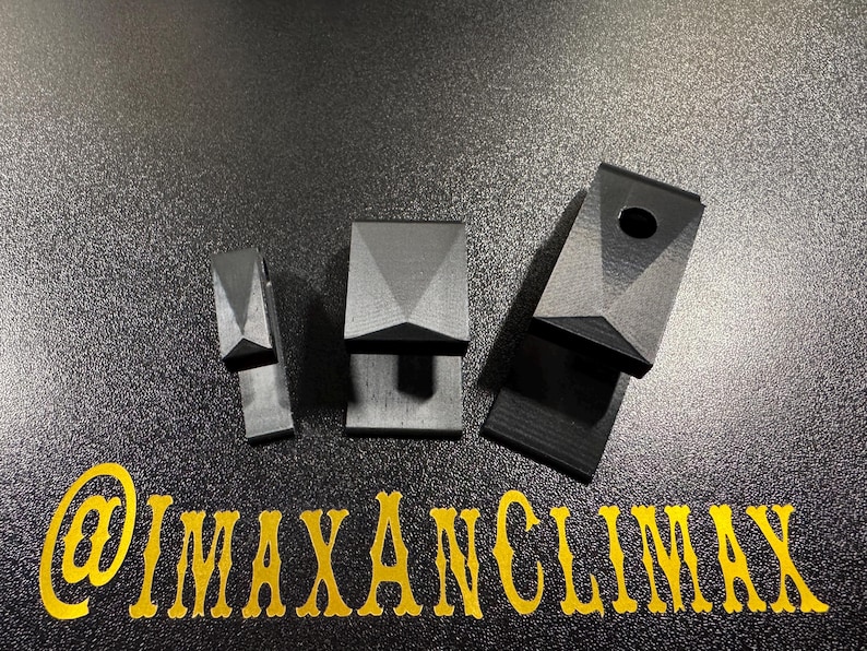 May include: Three black geometric objects with a faceted top and a rectangular base are displayed on a textured black surface. One object has a hole. The text "@IMAXANCLIMAX" is in gold script at the bottom.