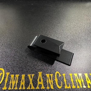 May include: A black metal money clip with a rectangular design and a circular hole. The clip is shown on a dark surface with the gold text "@IMAXANCLIMAX".